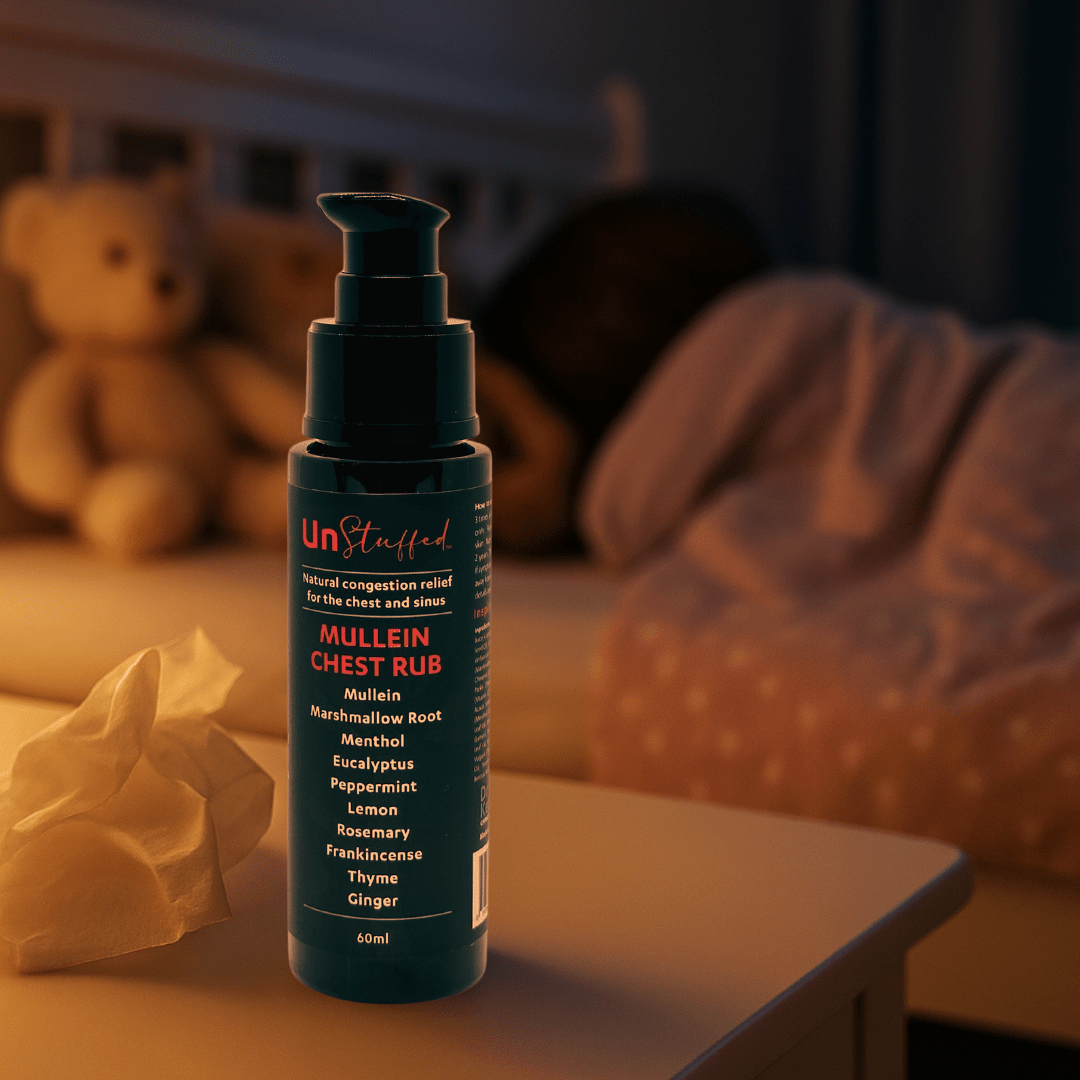 UnStuffed Mullein Chest Rub bottle on a surface with a teddy bear and blanket in the background